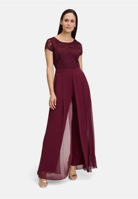 Bordeauxfarbener Jumpsuit mit Spitzen-Oberteil, kurzen Ärmeln und weit fließenden Hosen. Transparente Einsätze sorgen für Bewegung. Glatte Textur mit gefältelten Details.