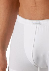 Boxer brevini bianchi in cotone con una vestibilità aderente, cintura elastica e un’etichetta cucita sul davanti. Texture liscia e senza motivi visibili.