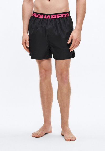 Schwarze Badehose mit einem pinkfarbenen elastischen Bund mit der Aufschrift "DSQUARED2". Der Stoff wirkt glatt und leicht, mit einem locker sitzenden Design.