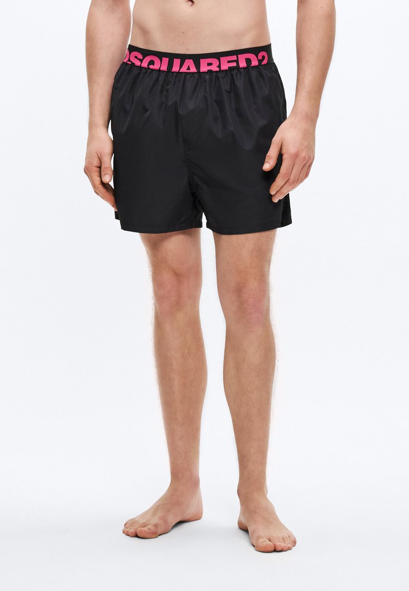 Slip de baie negri cu talie elastică roz inscripționată "DSQUARED2." Materialul pare neted și ușor, cu un design lejer.