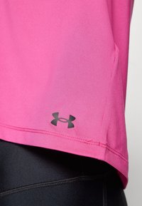 Närbild av en rosa träningströjas fåll med svart Under Armour-logotyp ovanför svarta träningsleggings.