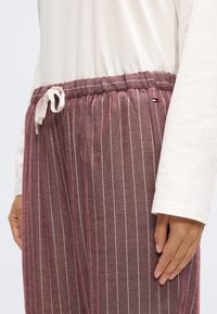 Bordošas svītrainas bikses ar aukliņu vidukļa daļā; mīksts materiāls; baltas vertikālas svītras un neliels logotipa akcents pie jostasvietas.