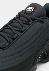 Dark grey sneaker with textured fabric upper, ribbed design, and flat laces. Features a black and red "Air Max" logo on the tongue.