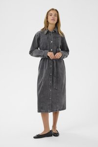 Grå denimklänning med långa ärmar, knappstängning framtill, bröstfickor och ett tygbälte. Platta svarta skor fulländar outfiten.
