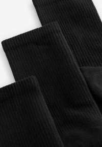 Schwarze, gerippte Socken mit einer weichen Textur, mittlerer Dicke und nahtlosem Design. Das Paar zeigt eine gleichmäßige, konsistente Farbe.