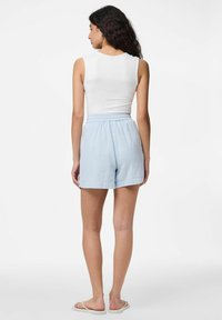 Gaiši zilas kokvilnas šorti ar elastīgu jostasvietu un brīvu piegriezumu, apvienoti ar pieguļošu baltu topi. Vienkāršs dizains, nav rakstu.