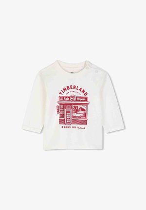 Wit lange mouwen peutershirt met rode Timberland winkelgrafiek en tekst, met een ontwerp van een laars en reparatiewerkplaats aan de voorkant.
