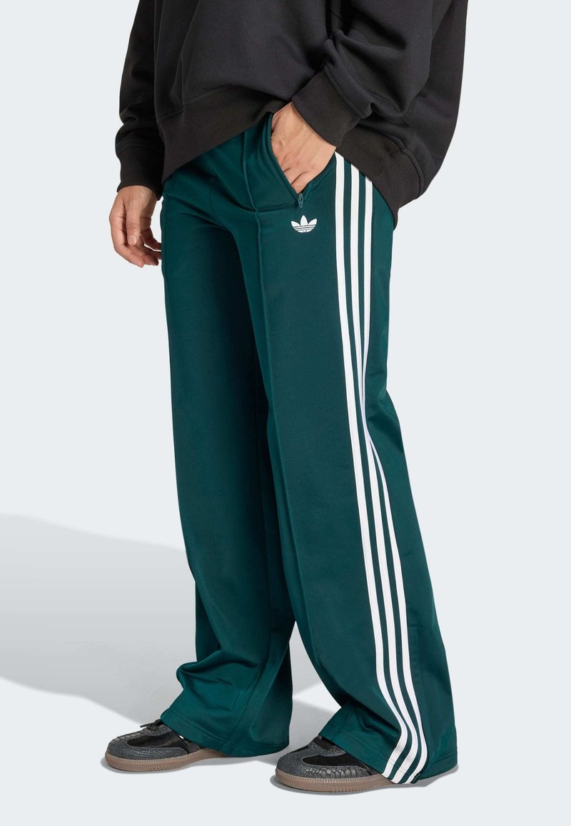 Dark green track pants featuring three white side stripes, zippered pockets, and a small logo. Made of smooth, lightweight fabric.
