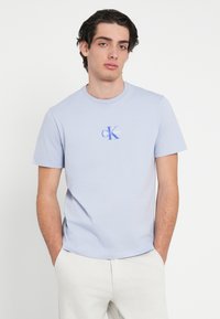 Ανοιχτό μπλε βαμβακερό t-shirt με μικρό μπλε λογότυπο "CK" και κείμενο, στρογγυλή λαιμόκοψη και κοντά μανίκια.