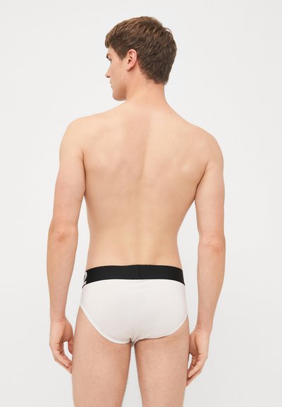 Culottes en coton blanc avec une taille élastique noire. Le design présente une texture lisse et une coupe ajustée, affichant un style minimaliste.