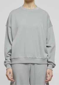 Sudadera gris claro de material suave, con cuello redondo, hombros caídos y puños y bajo acanalados para un ajuste cómodo.