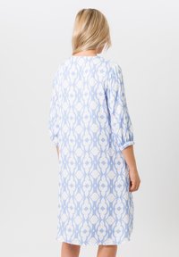 Helles blaues Kleid mit einem geometrischen weißen Muster, Dreiviertelärmeln und lockerem Schnitt. Weicher Stoff mit glatter Textur.