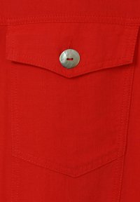 Rode stof met een gestructureerd oppervlak, voorzien van een borstzak met een afgeronde flap en een glanzende zilveren knoop voor sluiting.