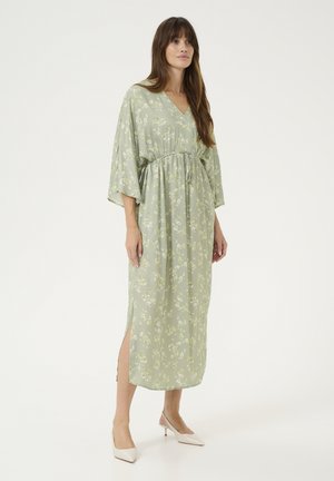 Abito lungo floreale di colore verde chiaro con scollatura a V, vita cin cinata e maniche ampie. Presenta spacchi laterali e una texture di tessuto fluido.