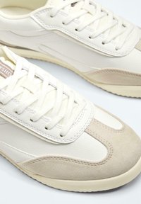Baskets décontractées blanches et beige à lacets, cuir texturé et panneaux en daim, vues de dessus et de côté.