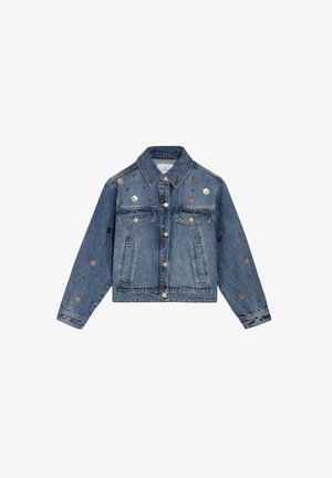 Veste en denim bleu avec un devant à boutons, deux poches poitrine, des poches latérales, et des clous métalliques circulaires dispersés sur le devant et les manches.
