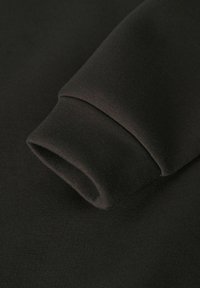 Melns sporta krekls ar mīkstu tekstūru; tam ir salocīts aproces ar gludu apdari un izturīgu šuvumu. Minimālistisks dizains.