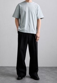 Světle modré bavlněné tričko s uvolněným střihem a krátkými rukávy, spárované s černými kalhotami širokého střihu a černými botami. Jednoduchý design, žádné vzory.
