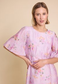 Lilla blomsterkjole med korte klokkeærmer, laget av lett stoff, med samlet midje og subtil teksturert mønster.