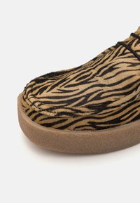 Slip-on sko med tigermønster i nyanser av brunt og svart, med en myk pelslignende tekstur og en lys brun gummisåle.