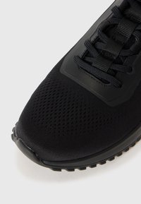 Zwarte sportieve schoen met een bovenwerk van mesh, versterkte neus, gestructureerd vetersysteem en een flexibele rubberen zool. Heeft een minimalistisch ontwerp en monochrome kleur.
