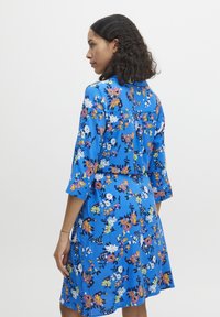 Rochie florală albastră cu mâneci trei sferturi, având flori și frunze multicolore, material ușor și croială ajustată.
