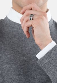 Maglione grigio a costine con una camicia bianca col colletto sotto. Anello d'argento con un design geometrico sul dito del modello. Ripresa ravvicinata.