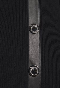 Svart ribbat tyg med en vertikal remsa av strukturerat svart läder som har två glänsande svarta knappar med silverfärgade cirkulära mönster.