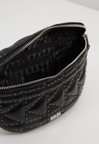 Mustikka tikattu nahkapussi hopea niiteillä, auki oleva vetoketju, sisäpuolella kuvioitu vuori ja hopea "KARL" -logo edessä.