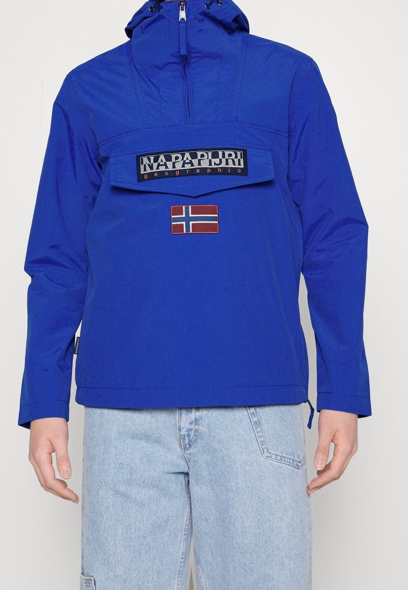 Modrá kapucňová bunda s přední kapsou, logem "Napapijri geographic" a nášivkou norské vlajky, nošená s světle modrými džíny.