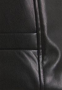 Matériau en cuir noir avec une surface texturée, présentant des détails cousus et un pli lisse et courbe. Fini légèrement brillant.