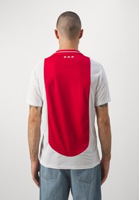 Maillot de foot avec un dos rouge, des côtés blancs et un col rond. Présente trois points blancs et une finition texturée sur le panneau arrière.