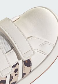 Scarpa in pelle bianca con cinturini in Velcro, caratterizzata da un design leopardato beige e marrone sul lato e dettagli in mesh bianco texturizzato.