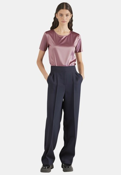 Top viola in raso a maniche corte abbinato a pantaloni a gamba larga blu navy a vita alta. Texture liscia e dettagli plissettati sui pantaloni.