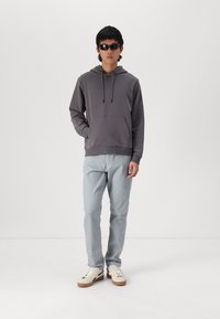 Grijze hoodie met drawstrings, een kangoeroezak, gecombineerd met lichtblauwe, iets gestructureerde broek en crèmekleurige sneakers met een bruine zool.