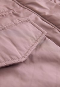Gros plan d'une poche en tissu rose poussiéreux avec des coutures détaillées sur un vêtement matelassé.