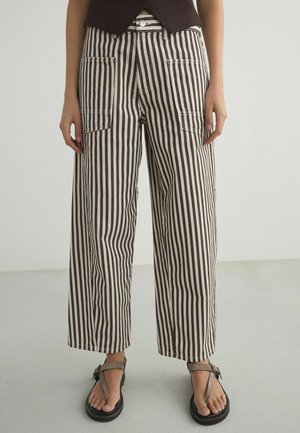 Leg-length view of person wearing wide-leg pants with vertical black and white stripes and open-toe sandals with ankle straps.