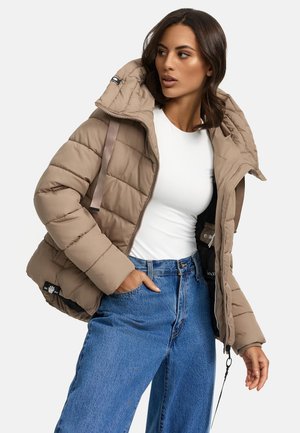 Tan pufferjack met een capuchon, horizontaal gequilt patroon, ritsluiting, zijzakken en tan kleurige banden. Draag het over een wit topje en een blauwe spijkerbroek.