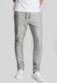 Pantalon de jogging gris avec taille à cordon, coupe fuselée, texture lisse, associé à des baskets blanches. Design simple, sans motifs visibles.