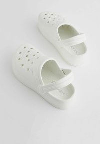 Sabots blancs dotés d'un design perforé, d'une sangle réglable et d'une semelle intérieure texturée. Fabriqués en matériau EVA léger pour plus de confort.