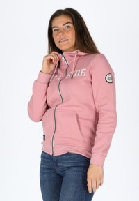 Felpa rosa con zip, cappuccio, tasche frontali e testo "SEA SIDE". Presenta polsini a coste e una toppa sul maniche sinistro. Tessuto morbido.
