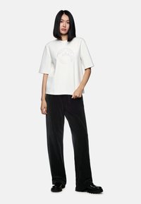 White short-sleeve t-shirt with a circular graphic design in gray, paired with black pinstripe wide-leg trousers and black shoes.
