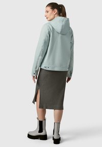 Giacca di jeans azzurro chiaro con cappuccio, abbinata a una gonna grigia a costine con uno spacco laterale. Stivali alla caviglia neri e grigi con suola spessa.