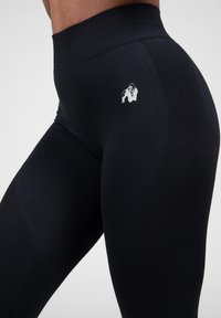 Black athletic leggings with a high waist, textured fabric, contrasting logo on the thigh, and fitted design for enhanced movement.