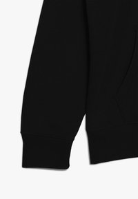 Puño de sudadera negra hecho de suave tela de algodón, con una textura acanalada y un acabado elástico, con un bolsillo lateral visible.