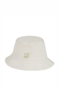 Een bucket hat van crème terrycloth, heeft een vlakke bovenkant en een brede, naar beneden hellende rand. Bevat een groen logo-patch aan de voorkant.