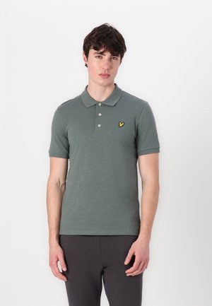 Polo en coton vert discret, doté d'un col, de manches courtes et d'une patte de boutonnage à trois boutons. Logo jaune notable sur la poitrine.
