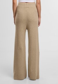 Beige široké kalhoty vyrobené z texturované pleteniny. Mají vysoký pas a spadají až k podlaze s volným střihem.