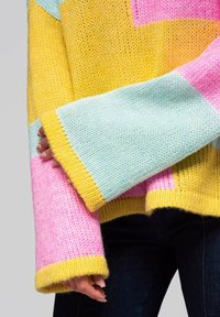 Brei trui met een geometrisch patchworkontwerp in geel, roze en teal. Losse mouwen met contrasterende geribde manchetten. Zachte textuur.