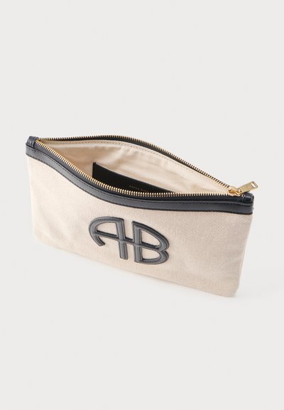 Béžové látkové puzdro s čiernym lemovaním, zlatým zipsom a vyrazeným čiernym logom "AB" na prednej strane, čiastočne otvorené, odhaľujúce vnútornú podšívku.